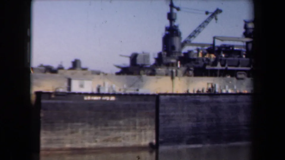 1946 Netherlands frame showing the side of a military vessel behind a harbor wall, with deck gun mounts, mast, crane, and water in front.