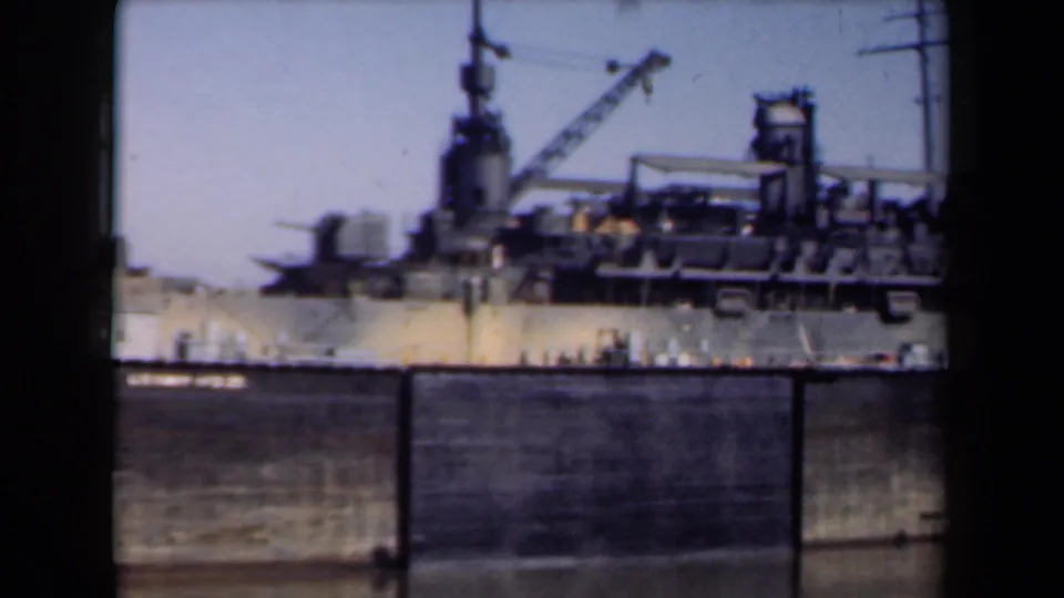 1946 Netherlands home-movie frame showing a docked military vessel in side view, with crane, mast, deck equipment, harbor wall, and water.