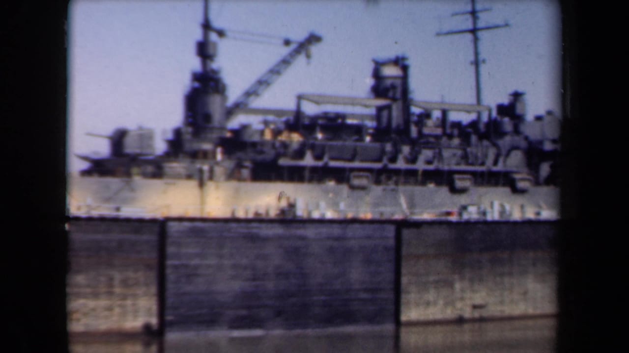 1946 Netherlands 8mm frame showing a large docked ship behind a quay wall, with cranes, mastwork, and deck structures visible.