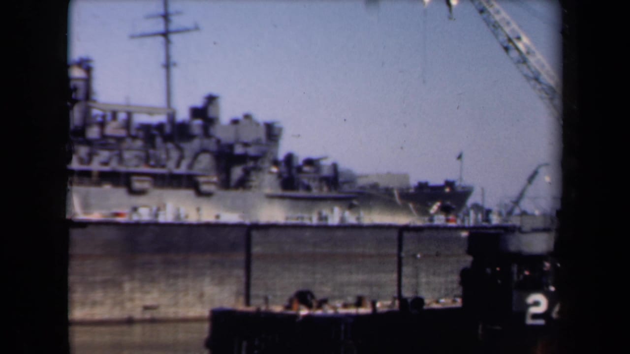 1946 Netherlands home-movie frame showing a large vessel, dockside cranes, and boat structure from a river journey viewpoint.