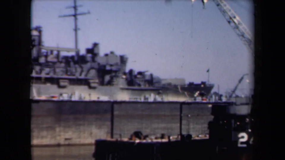 1946 Netherlands home-movie frame showing a large vessel, dockside cranes, and boat structure from a river journey viewpoint.