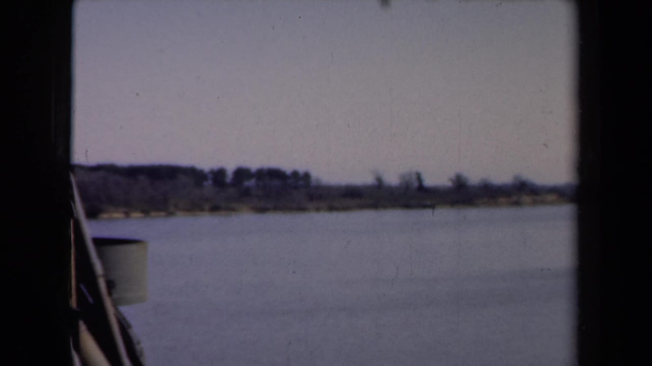 1946 Netherlands river view from a boat, with calm water, a low wooded shoreline, and pale sky.
