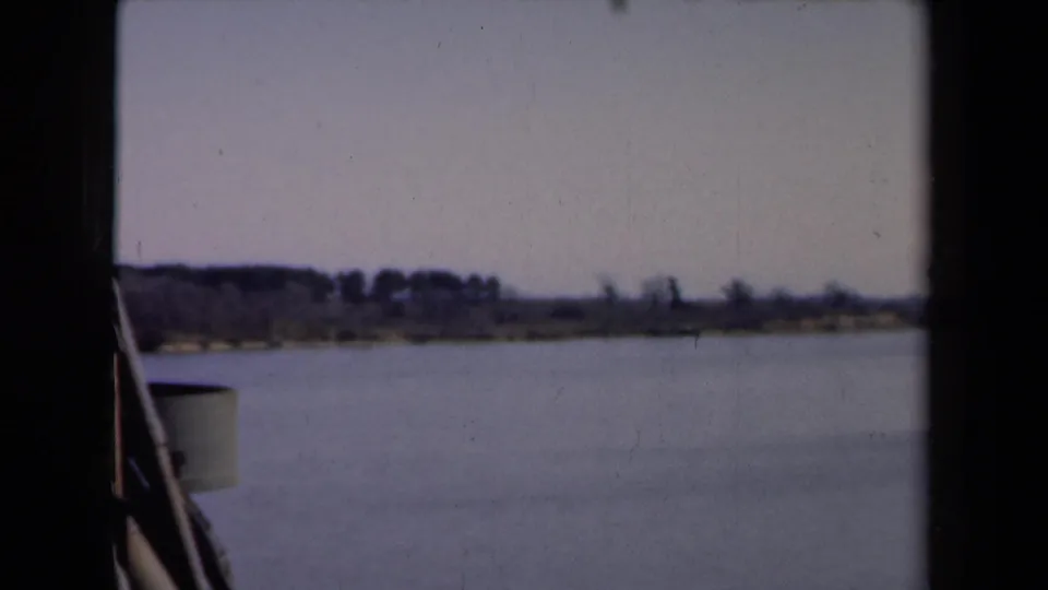 1946 Netherlands river view from a boat, with calm water, a low wooded shoreline, and pale sky.