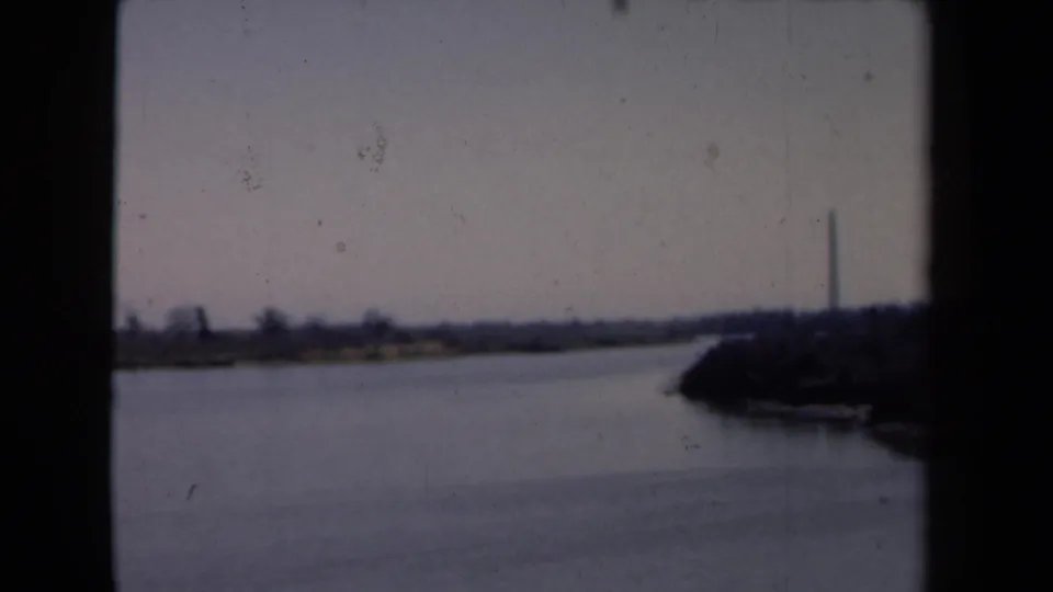 Final 1946 Netherlands frame showing calm water, distant shoreline, dark right bank, and a tall slender tower or monument.