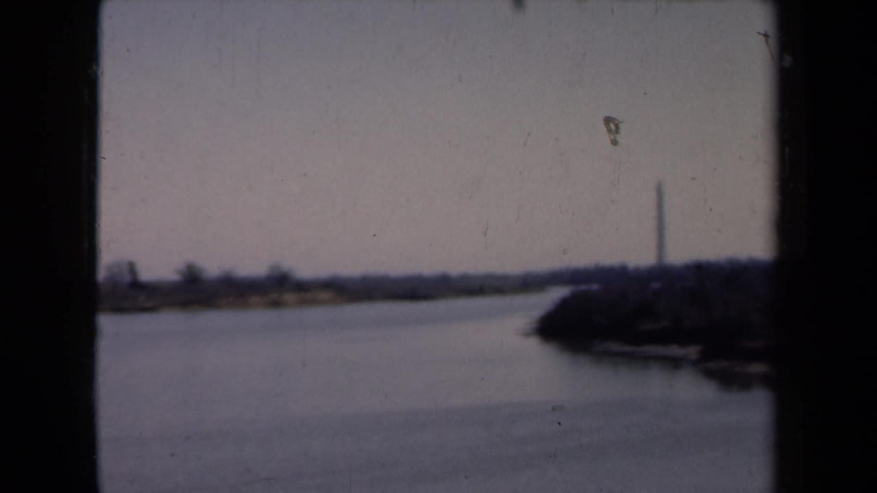 Soft 8mm view across a waterway with a distant obelisk-like monument and dark shoreline.
