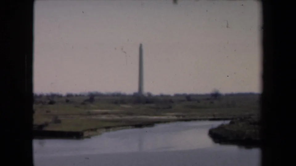 A wide 8mm frame shows the distant monument across water, bordered by dark film edges and muted color.