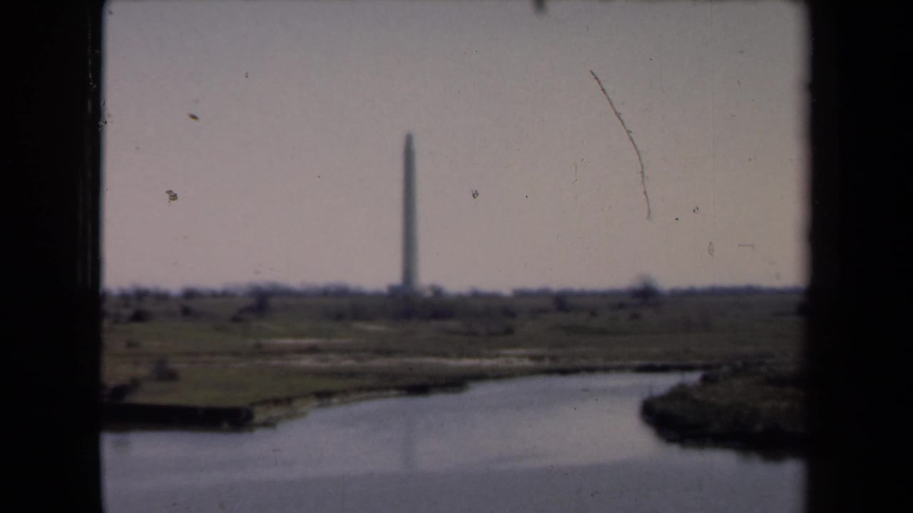 Distant tall monument beyond a wide body of water, framed by dark vertical edges.