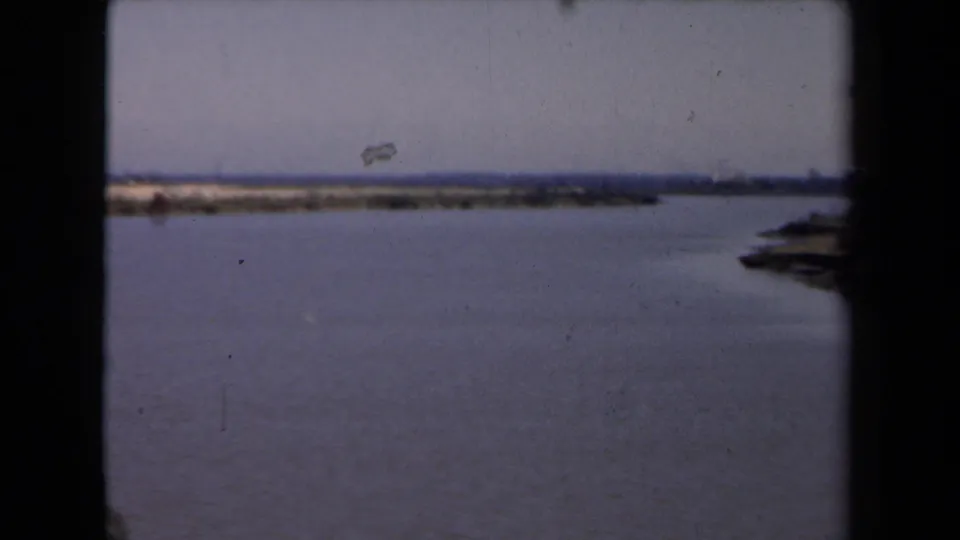 1946 8mm home-movie frame showing a broad water surface, low distant shoreline, and dark structural framing in the foreground.