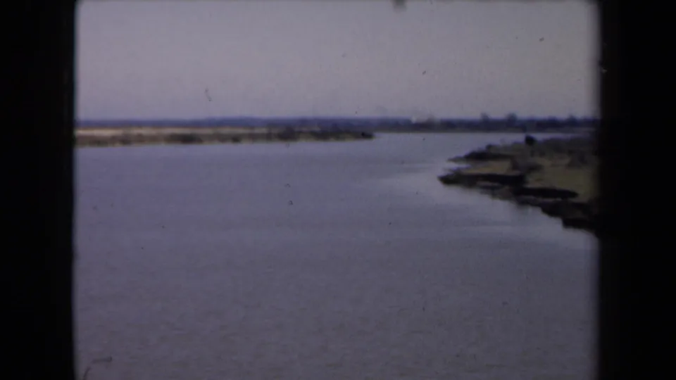 Final 1946 8mm frame showing a quiet waterway, low horizon, and shoreline detail, with the dark frame edge still visible.