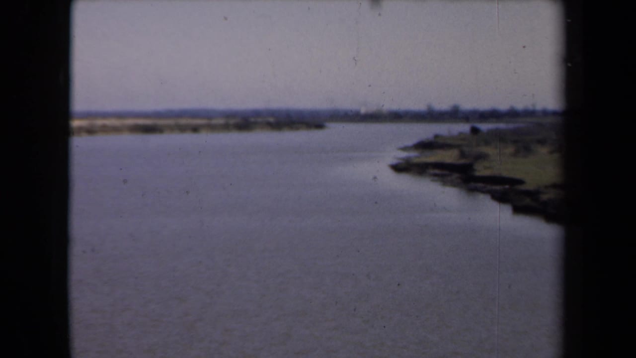 Calm water beside a low green shoreline under a cloudy sky.