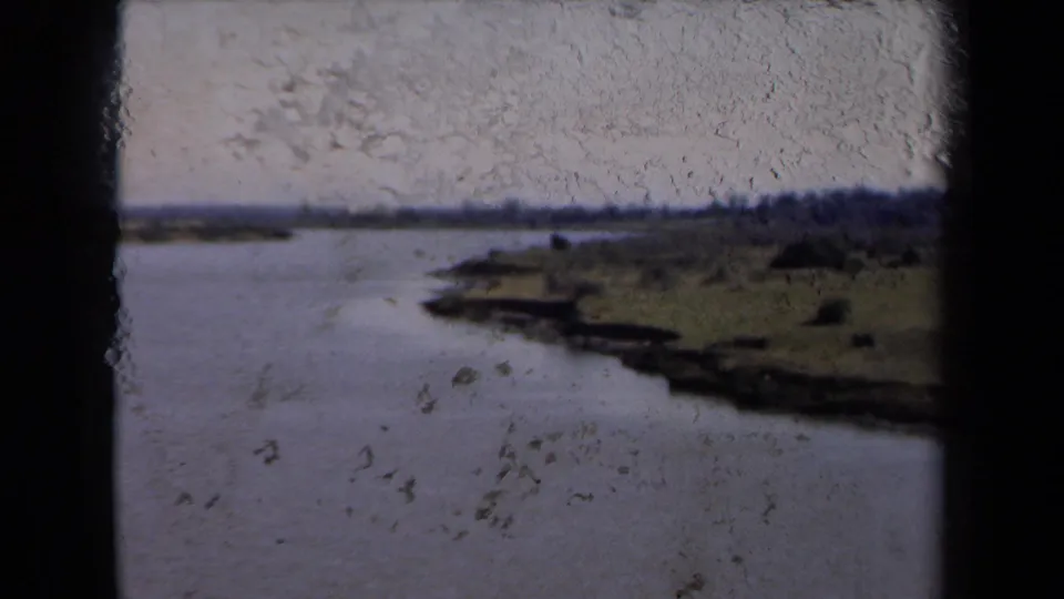 1946 Netherlands 8mm frame showing calm water and green shoreline with heavy visible dust, scuffing, and exposure variation.