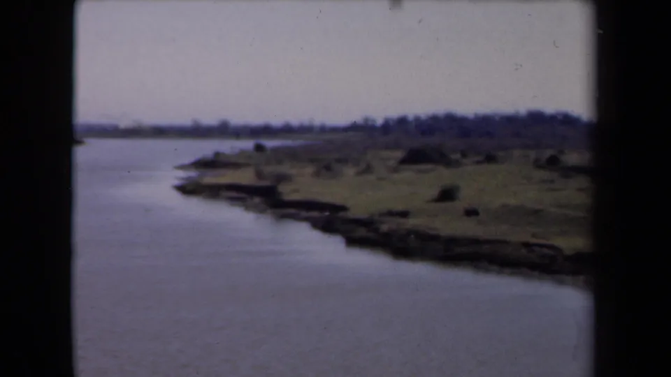 1946 Netherlands 8mm frame with calm water, a curved low shoreline, sparse vegetation, and an overcast sky.