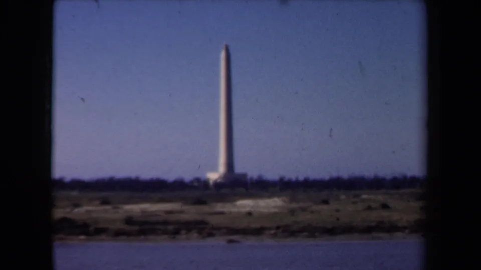 1946 Netherlands 8mm frame with a distant slender tower, low shoreline, calm water, and a muted blue sky in soft focus.