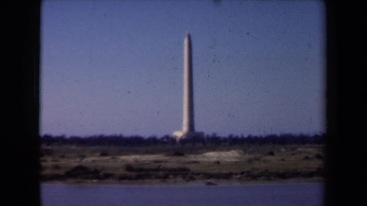 Distant tall monument across water under a clear sky.