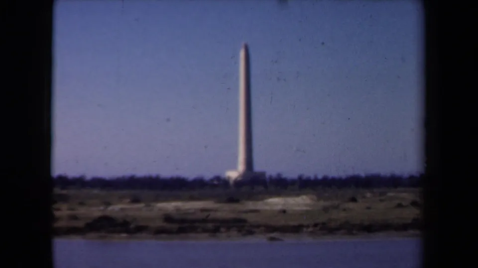 1946 Netherlands 8mm frame showing a distant obelisk-like monument across calm water with low shoreline detail.