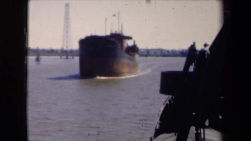 Large ship moves across calm water in a 1946 Netherlands 8mm frame, with waterfront towers and dark railing silhouettes nearby.