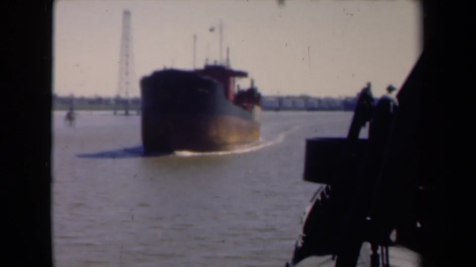 The ship continues past on the water, with distant waterfront structures and foreground silhouettes in the 1946 Netherlands home movie.