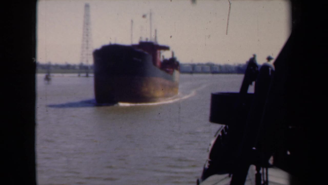 1946 Netherlands 8mm frame of a dark barge moving through harbor water, with a distant derrick and silhouetted foreground deck structure.