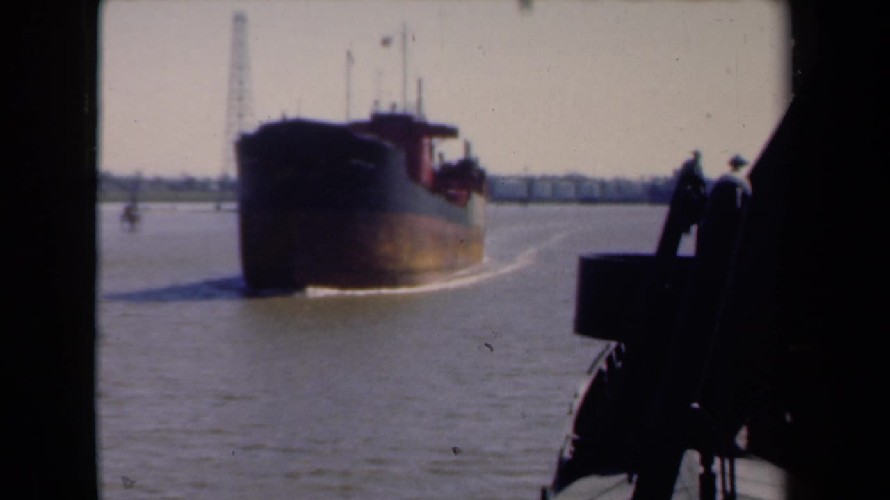 1946 Netherlands harbor view showing a commercial barge under way, distant waterfront structures, and a dark boat edge in the foreground.