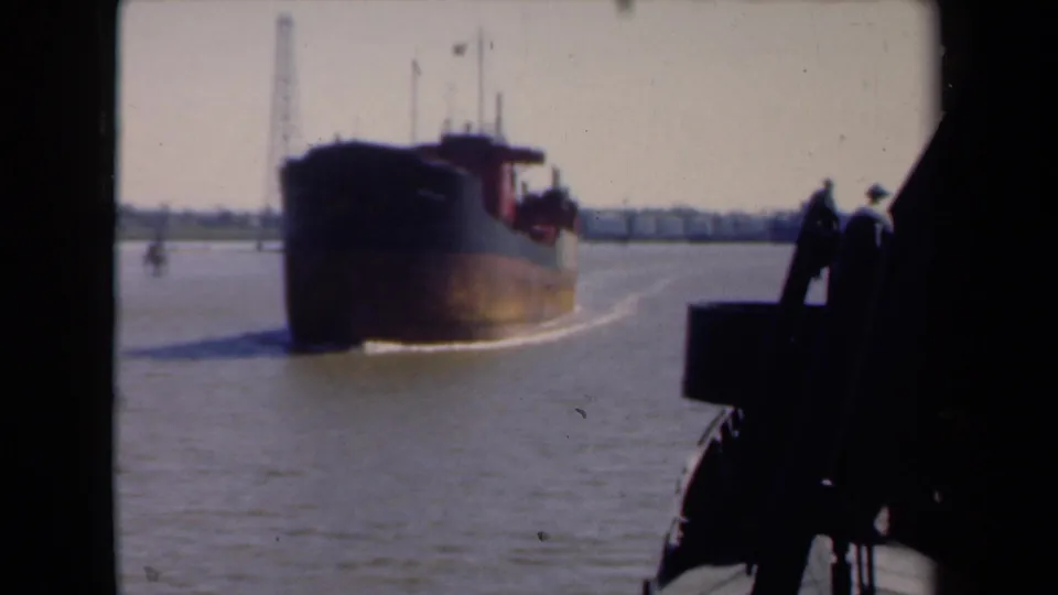 1946 Netherlands harbor view showing a commercial barge under way, distant waterfront structures, and a dark boat edge in the foreground.