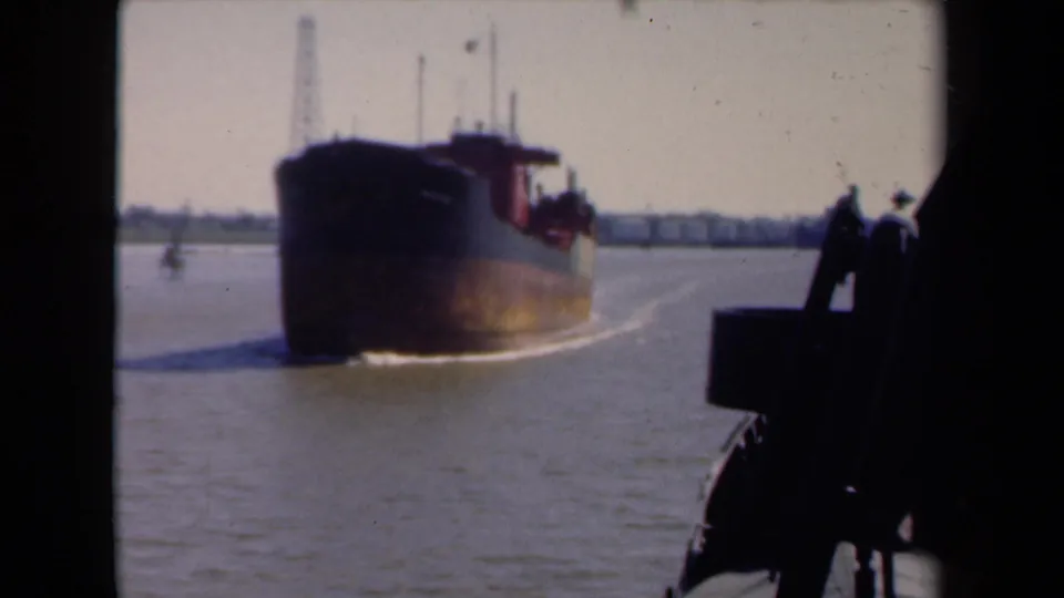 Soft 8mm frame from 1946 Netherlands showing a barge moving across a harbor, framed by dark boat fittings in the foreground.