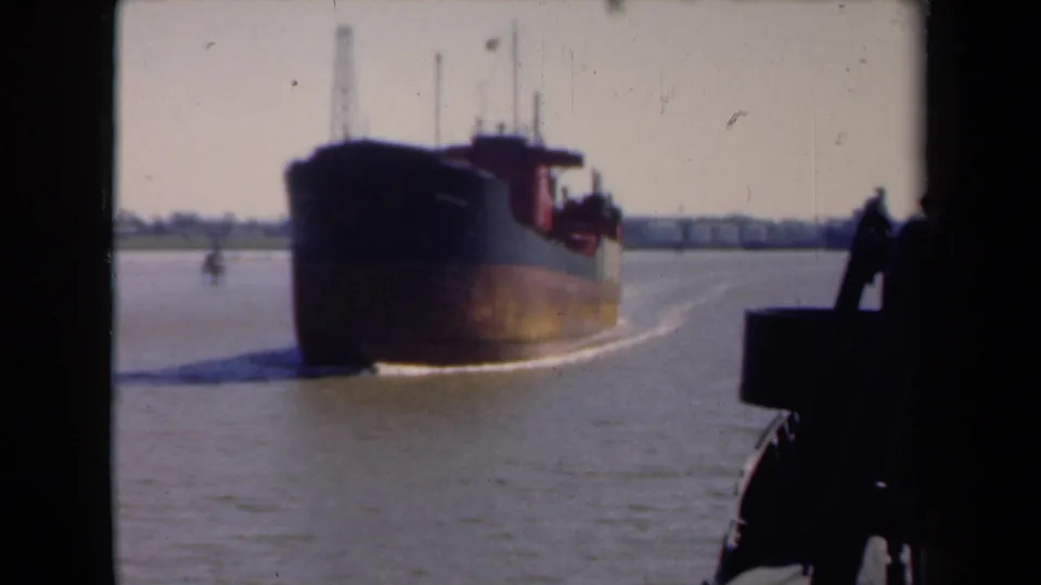 1946 Netherlands 8mm harbor frame with a dark commercial barge, red upper structure, wake, and silhouetted foreground vessel detail.