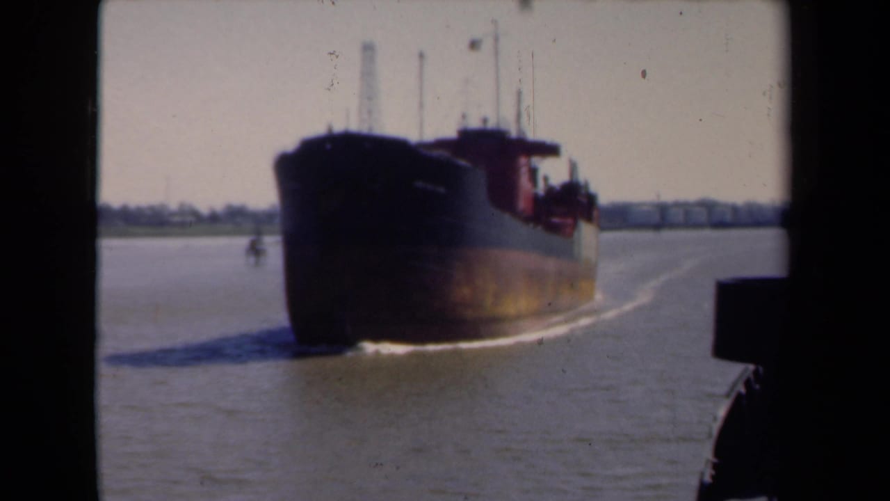 Cargo ship on river water with a pale sky and shoreline in the distance.