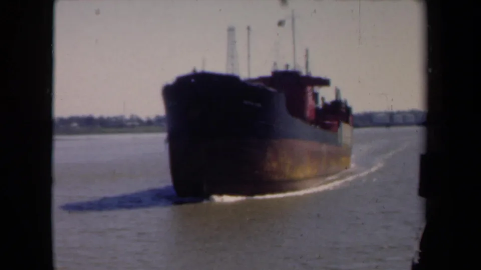 The cargo ship fills more of the frame as it passes on the river, with a dark hull, red upper structure, and distant Netherlands shoreline.