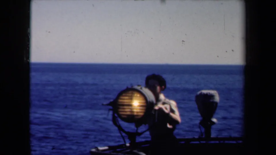 1946 Netherlands 8mm frame with a sailor near a glowing signal light on deck, framed by open water and horizon.