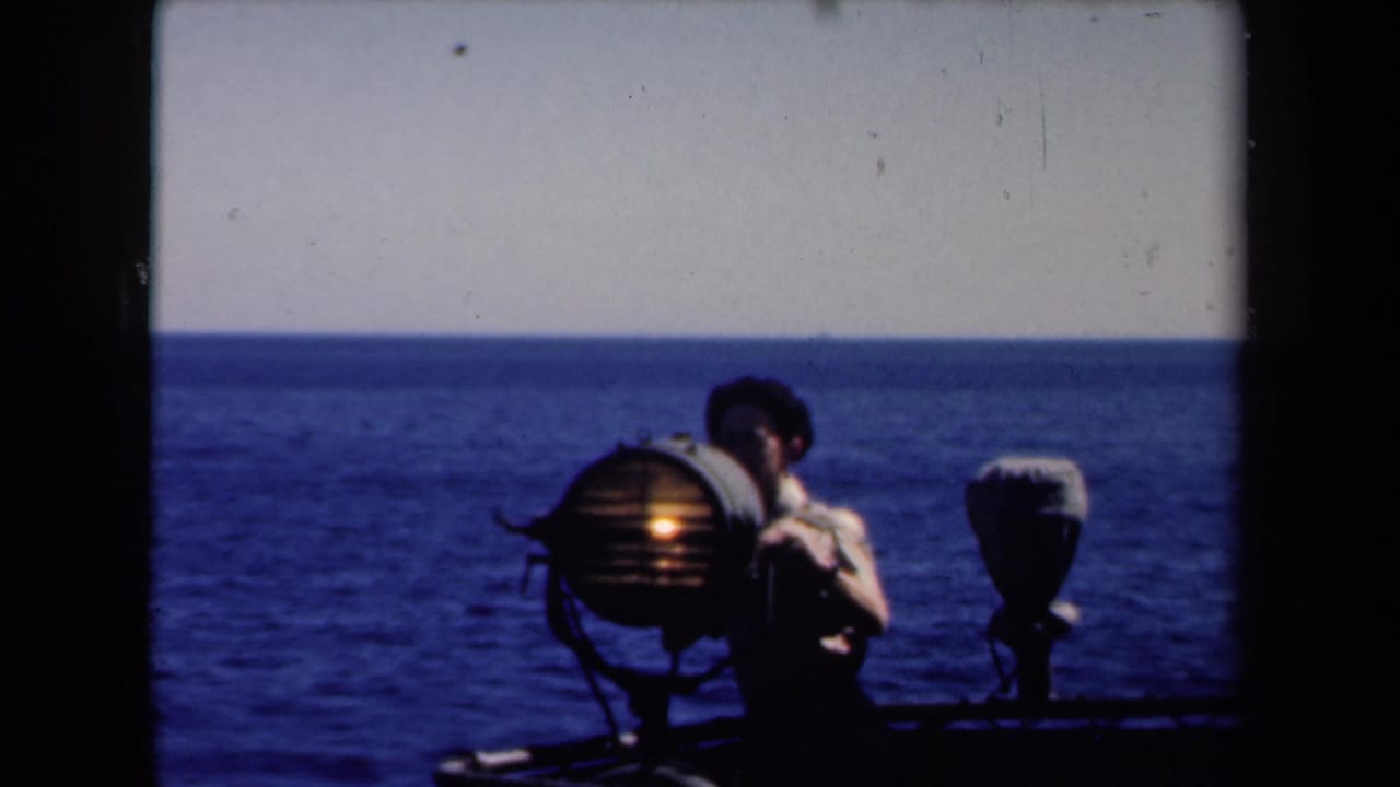 Young man beside an illuminated shipboard searchlight with open sea behind him.