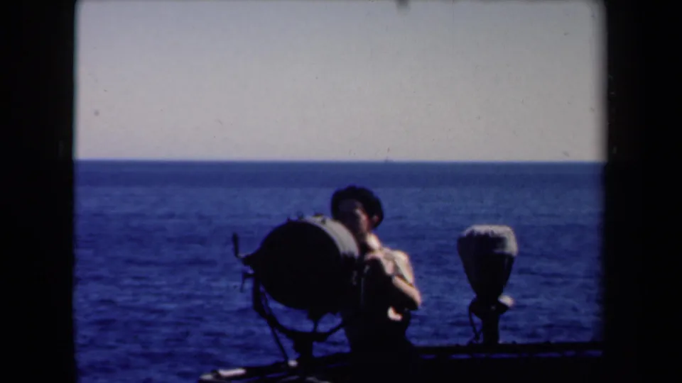 The young man remains beside the shipboard searchlight, silhouetted against the blue sea and pale horizon in 1946 Netherlands footage.