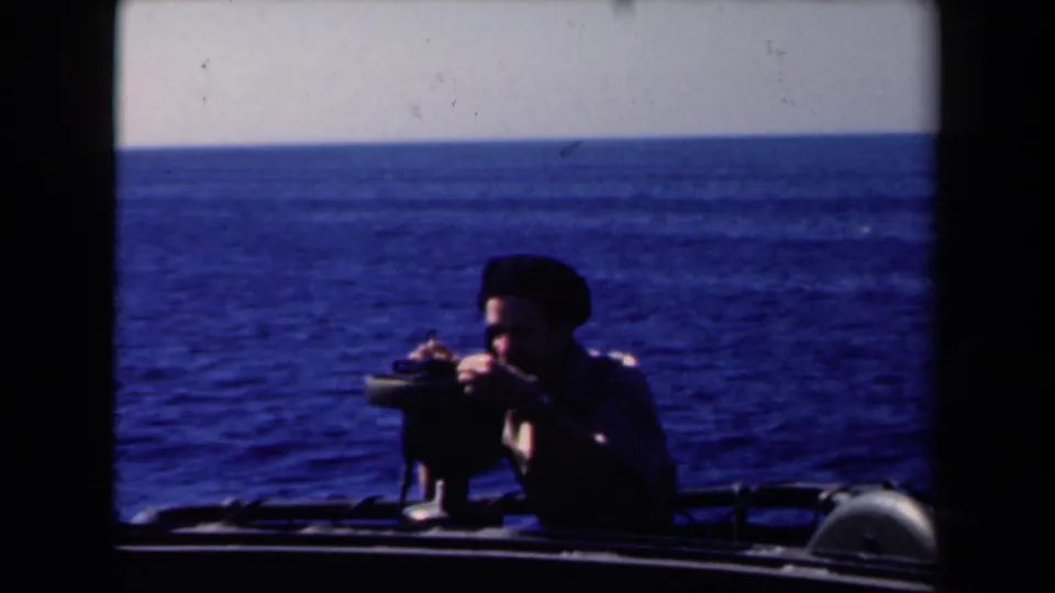 In 1946 Netherlands footage, a man in a dark beret uses a mounted optical device aboard a boat against dark blue water.