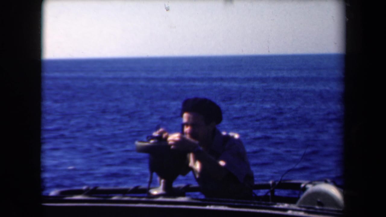Man keeps his face close to a mounted device while standing or sitting low on a boat at sea.