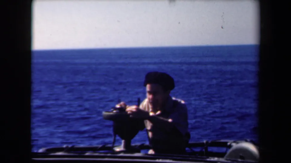 In the final frame, the man in a beret continues using the mounted device on the vessel, with open sea behind him.