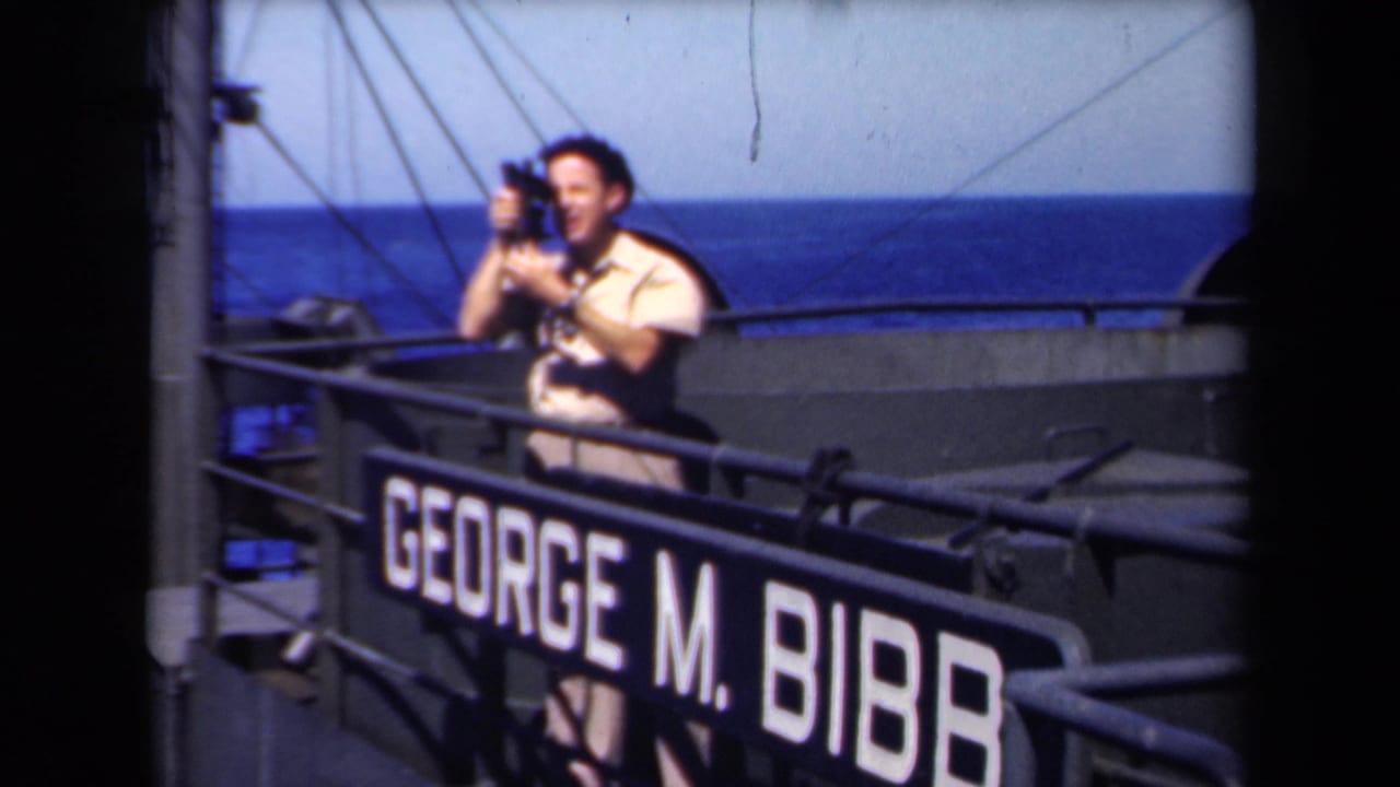 Young seaman on a ship deck holds a small camera above a George M. Bibb nameplate.