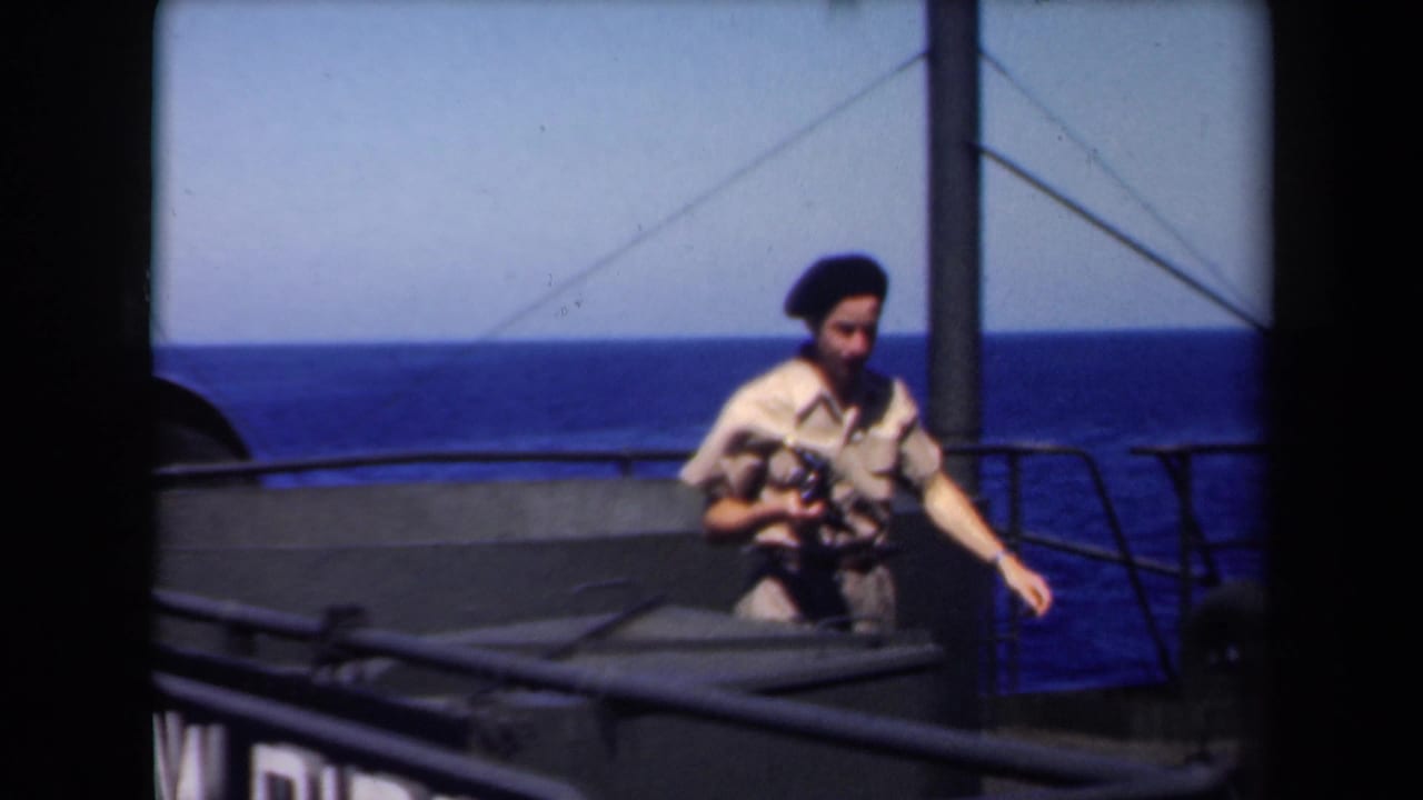 1946 Netherlands home-movie frame of a khaki-clad sailor in a dark beret holding a camera on a ship deck at sea.