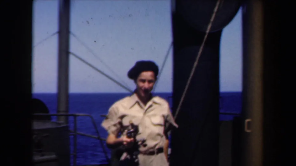 1946 Netherlands frame of a smiling sailor in khaki uniform and dark beret holding a camera beside ship railings.