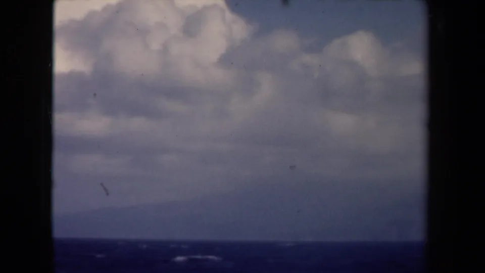 1946 Netherlands 8mm frame showing a broad cloud bank, blue water, and a darker distant horizon or landform.