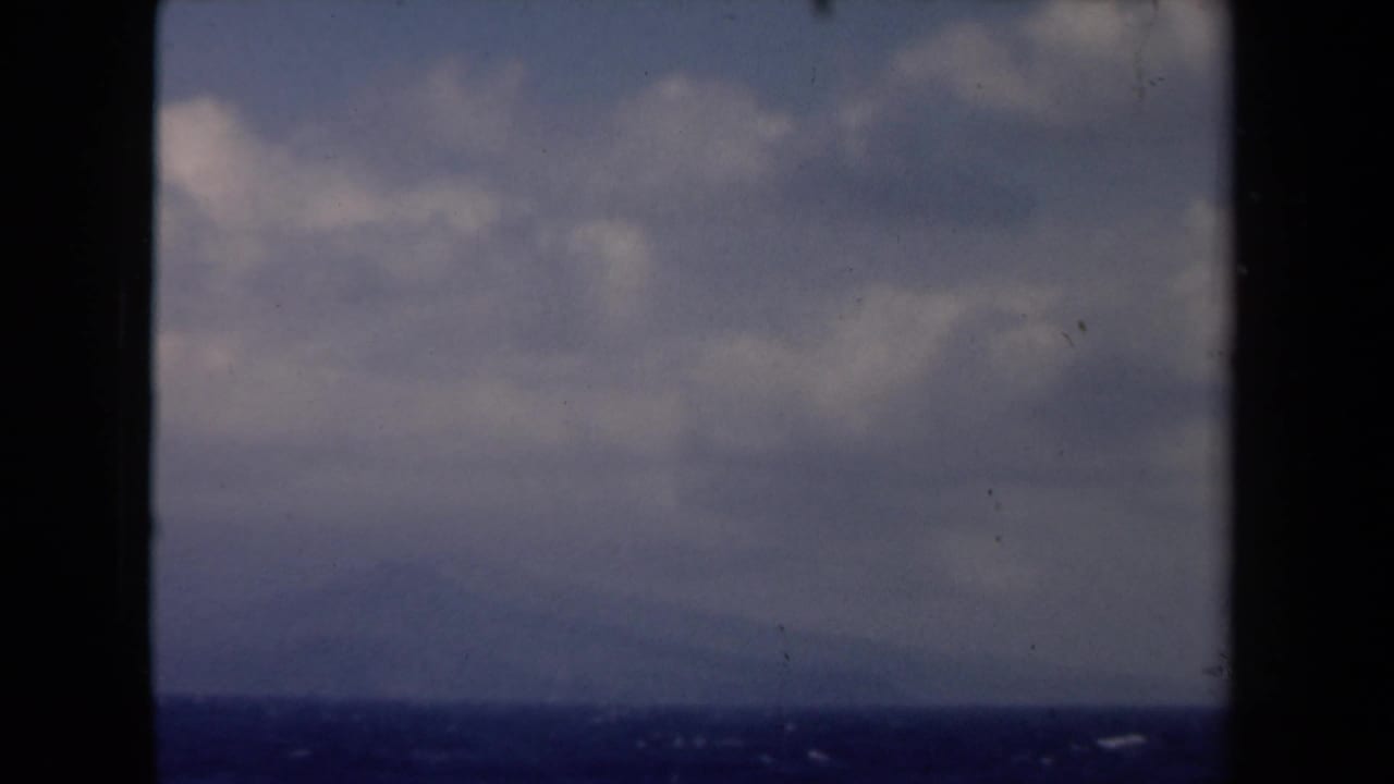 Cloudy sky and distant shoreline seen through dark vessel window framing.