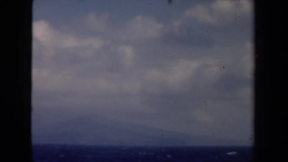 1946 Netherlands 8mm frame showing blue water, a hazy low shoreline, and clouded sky through dark window mullions.