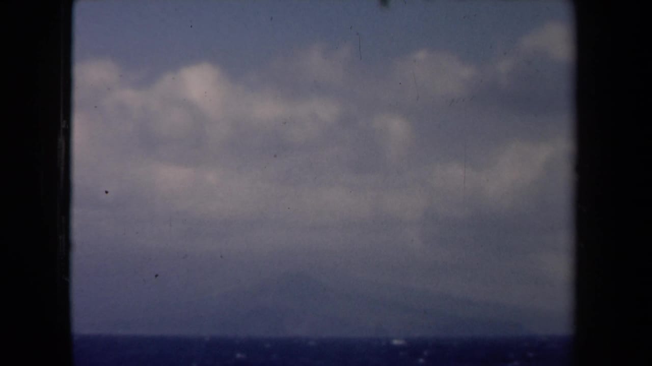 Hazy horizon and clouds over water framed by dark vertical window edges.