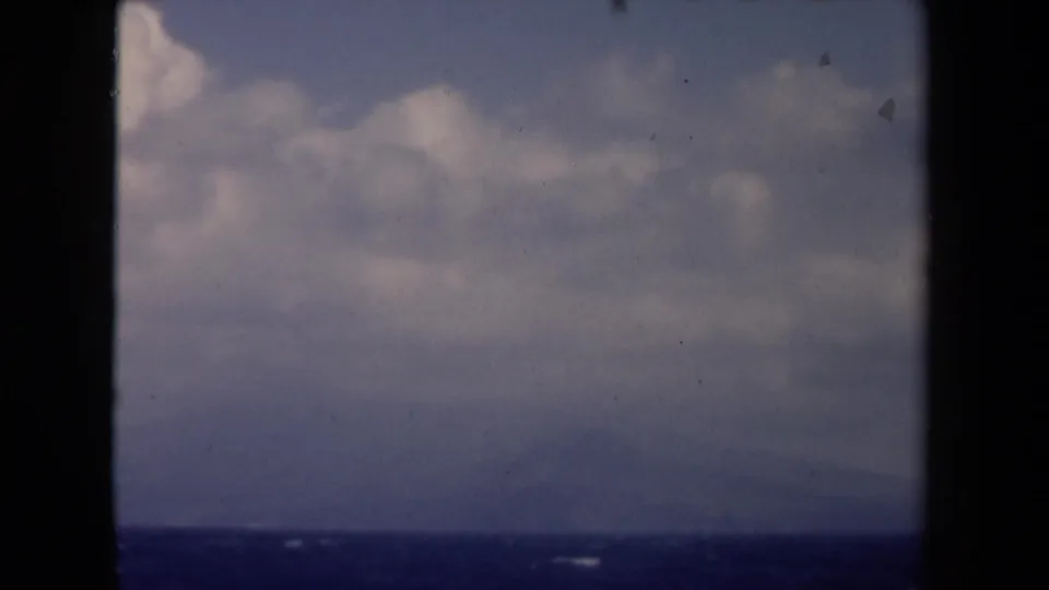 1946 Netherlands 8mm still showing blue sea, broad clouds, dark window bars, and a faint distant coast.