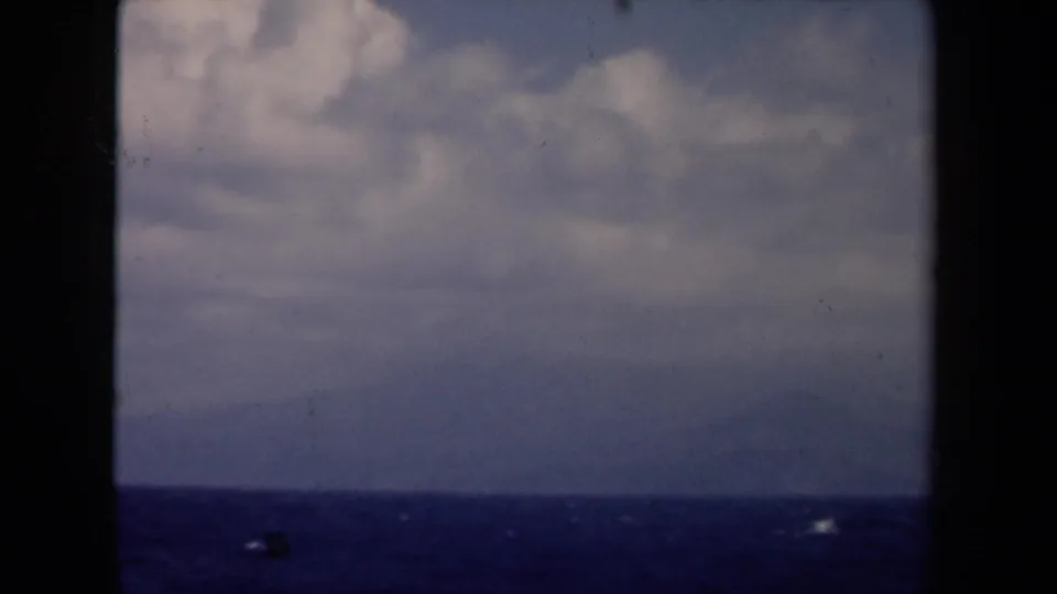 1946 Netherlands 8mm frame with a clouded sky, deep blue water, and faint shoreline viewed through vessel-window bars.