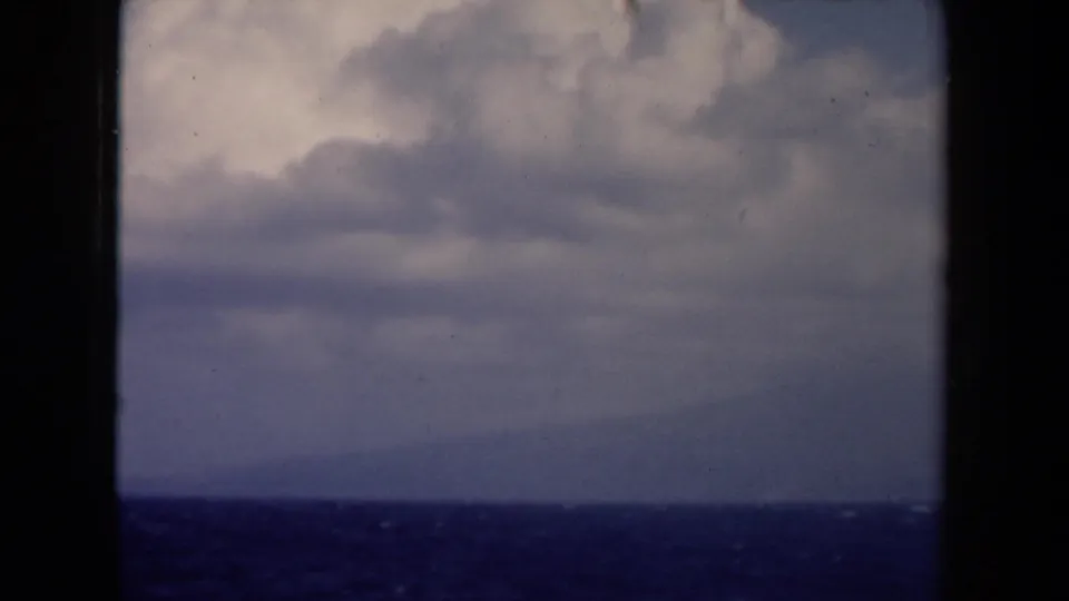 1940s Netherlands home-movie frame of open water and distant horizon beneath layered clouds from a moving vessel.