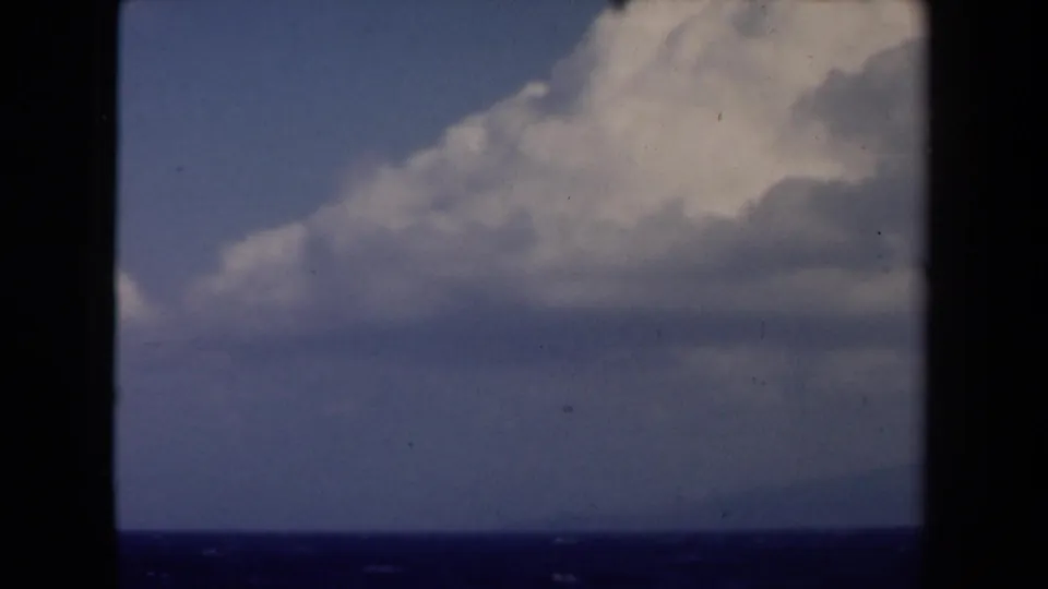 1946 Netherlands 8mm view of bright clouds over a dark sea horizon, with faint land or island shapes in the distance.