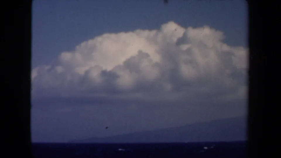 1946 Netherlands 8mm frame with an island or low shoreline across blue water beneath a bright, towering cloud bank.