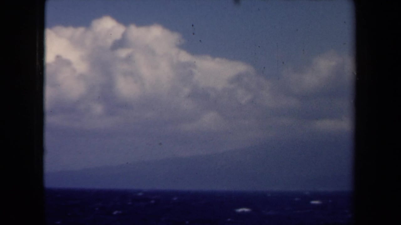 1946 Netherlands 8mm frame with deep blue water, distant hazy land, and towering clouds across the sky.