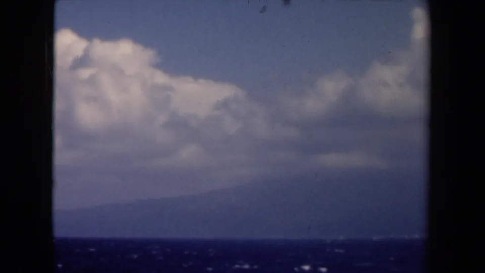 1946 Netherlands 8mm frame showing a low sea horizon, soft distant land, and bright clouds drifting above.
