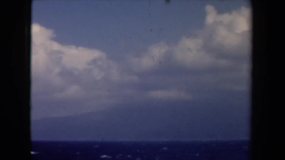 1946 Netherlands 8mm frame of open sea, distant hazy land, and broad cumulus clouds within dark film edges.