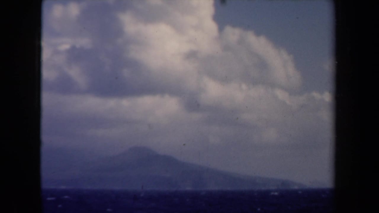 1946 Netherlands 8mm frame with a hazy distant landform across open water beneath billowing clouds.